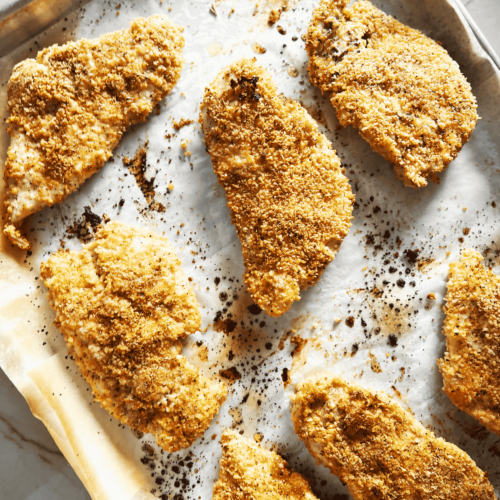 Seven pieces of baked breaded chicken on a baking sheet.