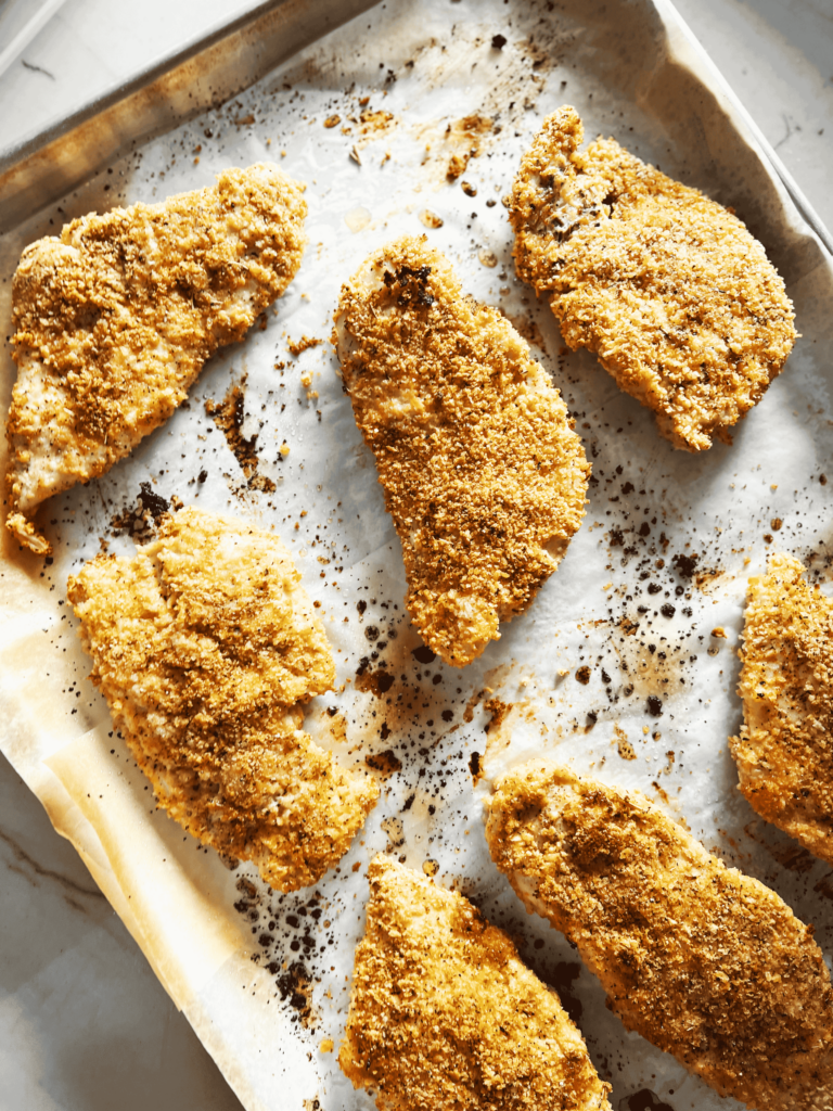 Seven pieces of baked breaded chicken on a baking sheet.
