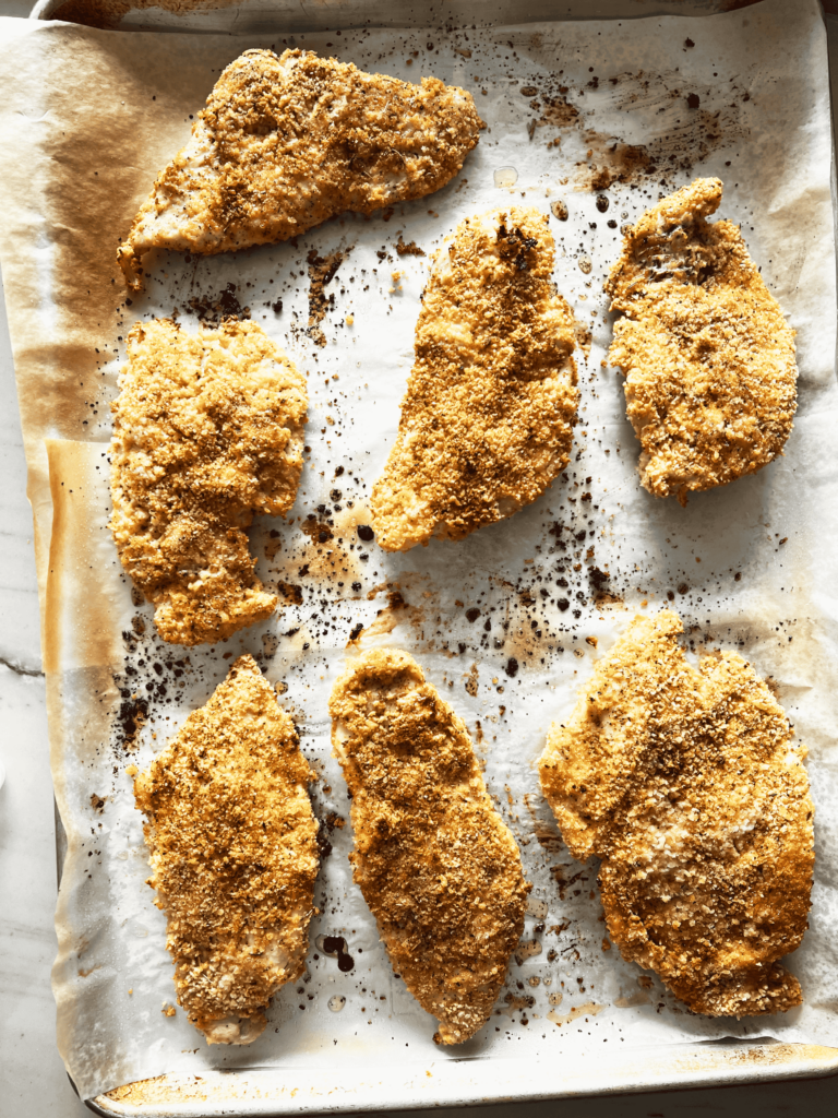 A baking sheet filled with breaded baked chicken breasts.