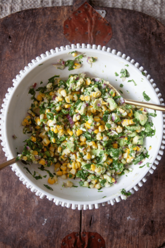 Corn avocado salad in large white bowl with two spoons.