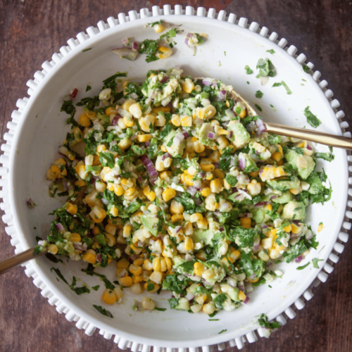 Corn avocado salad in large white bowl with two spoons.