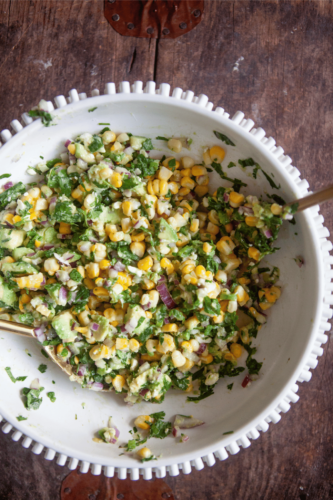 Corn and avocado salad with red onions and cilantro in a large bowl.