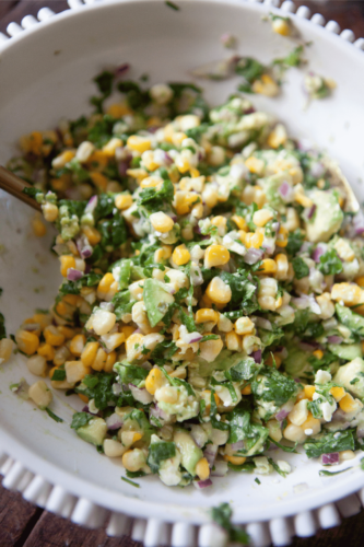 Corn, avocados, cilantro, and red onion for avocado corn salad in a bowl.