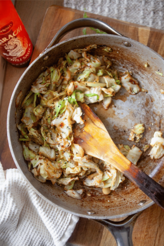 Sautéed cabbage with a bottle of sriracha next to it.