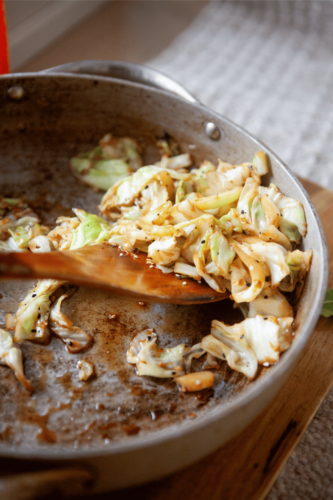A wooden spoon stirring a sautéed cabbage recipe.