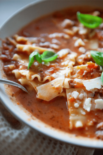 A spoon in a bowl of low-carb lasagna soup in a white bowl.