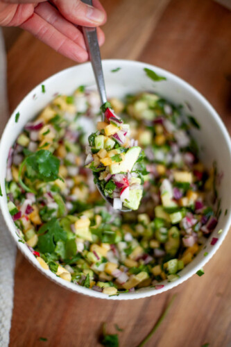 A close up of a spoonful of pineapple radish salsa with diced pineapple and diced jalapeno.