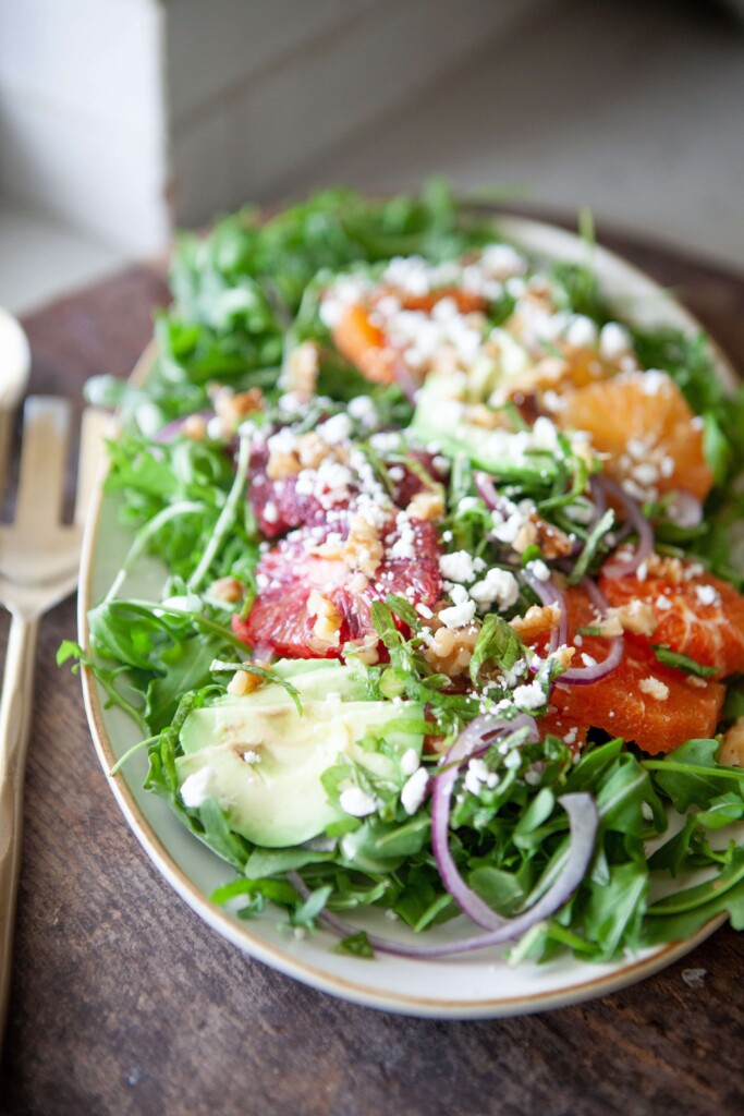 Winter citrus salad in large white serving bowl with two serving spoons on table.