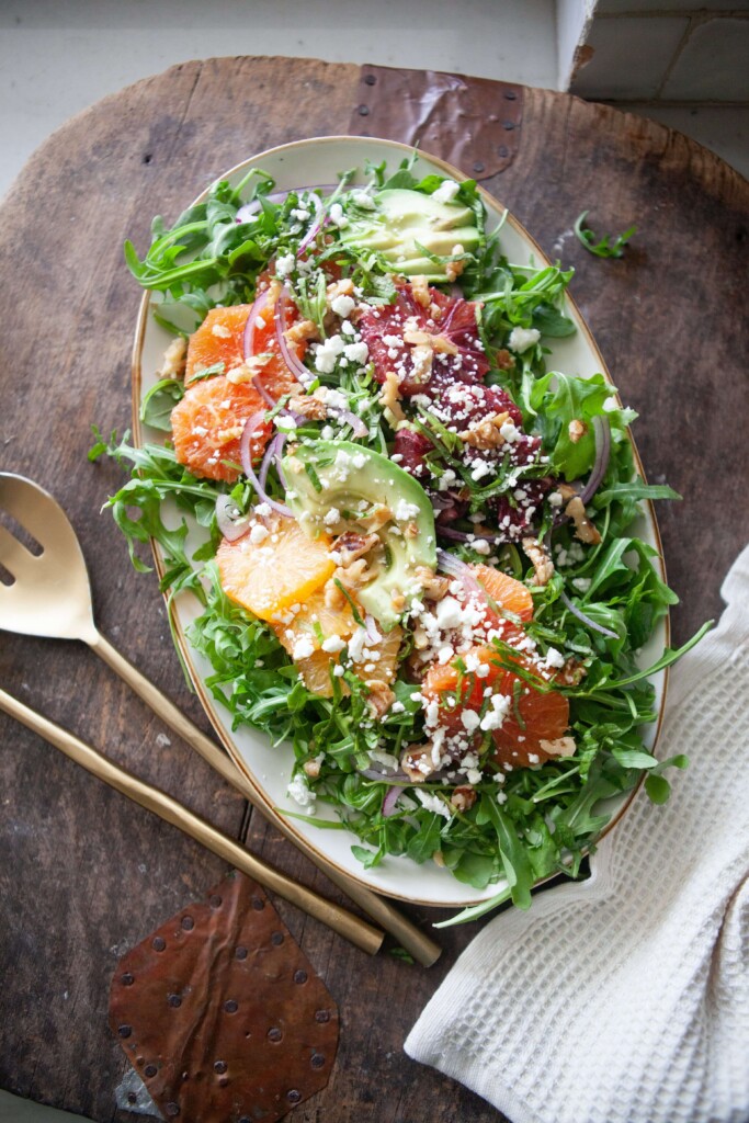 Winter citrus salad in large white serving bowl with two serving spoons on table.