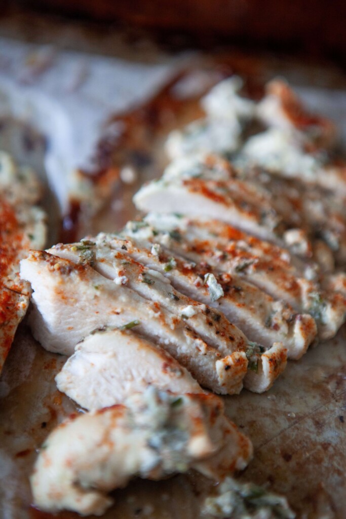 Sliced yogurt and herb chicken breasts on parchment tray.