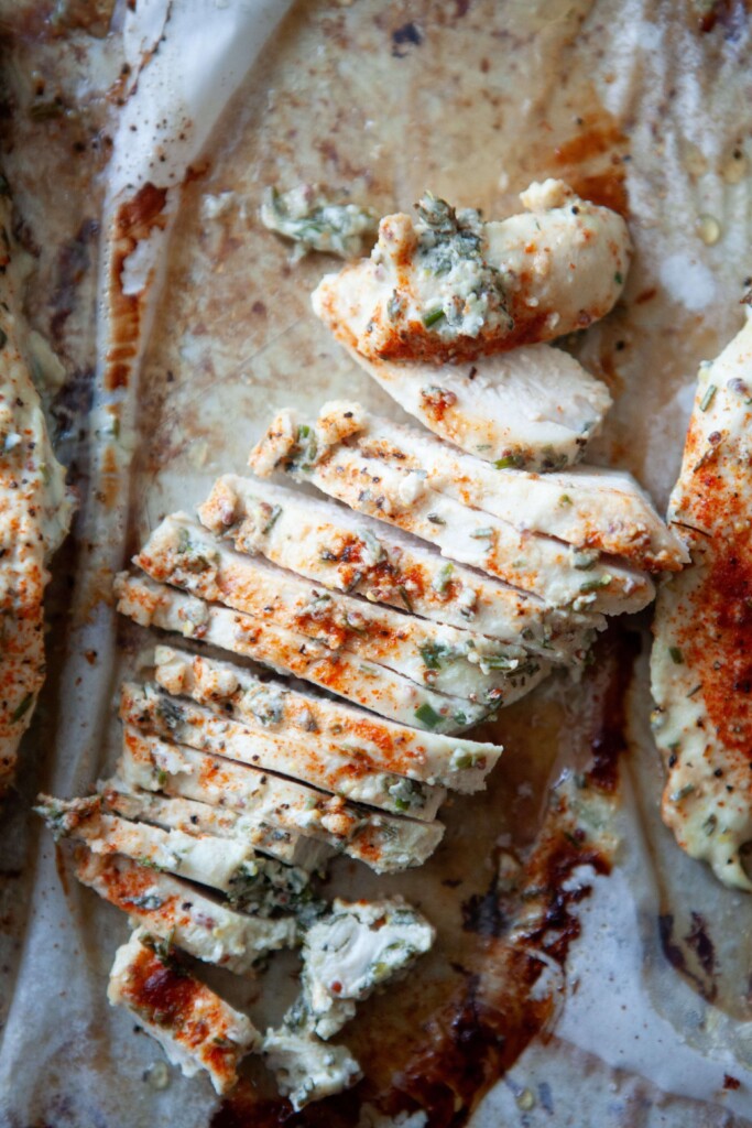 Sliced baked yogurt and herb chicken breasts on parchment paper.