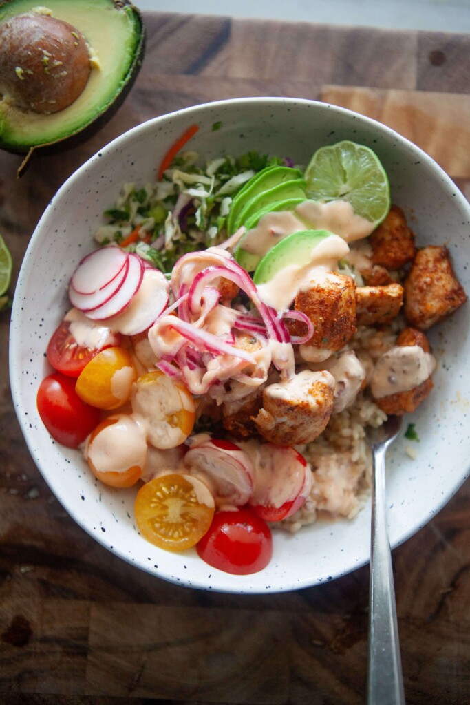 Mahi mahi fish taco bowl in white bowl with fork on wooden cutting board.