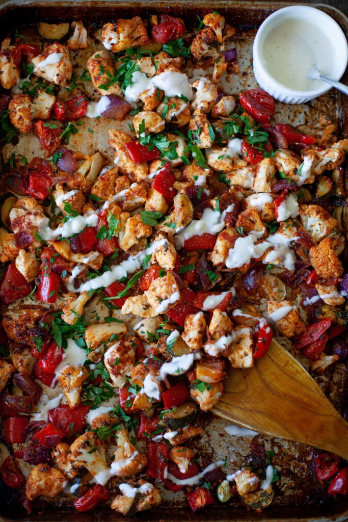 Harissa chicken drizzled with creamy hummus sauce on sheet pan garnished with parsley.