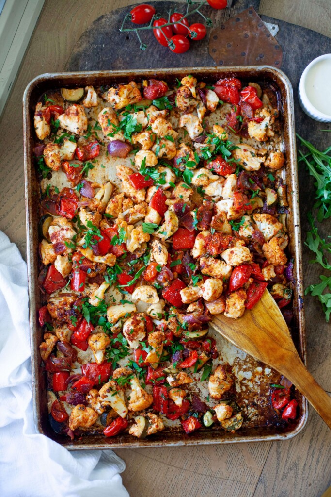 Harissa chicken and vegetables garnished with parsley on sheet pan with wooden spoon.