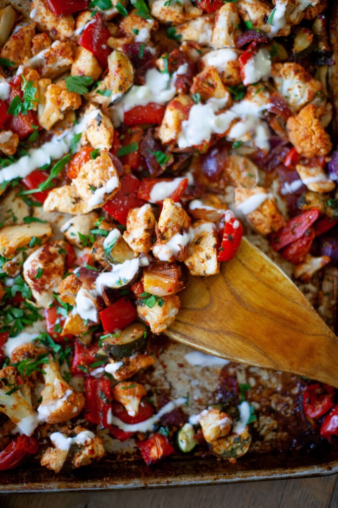 Harissa chicken drizzled with hummus sauce on sheet pan with wooden spoon.