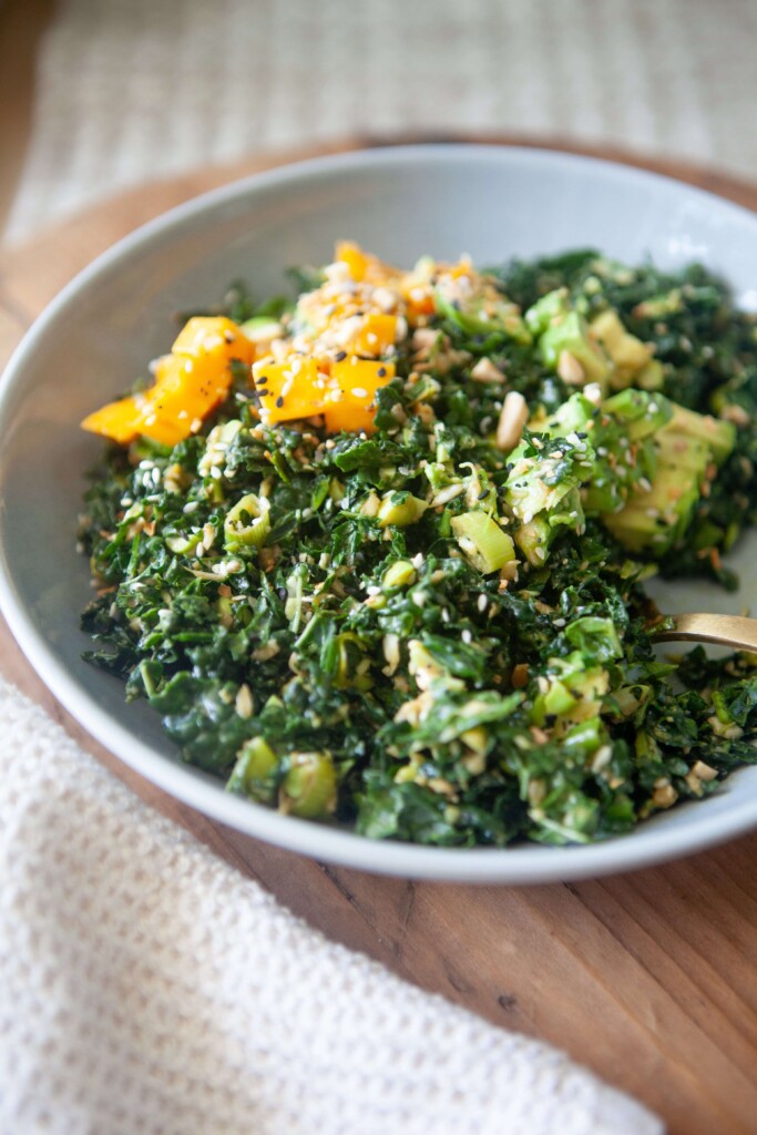 Chopped kale salad with peanut vinaigrette in white bowl with gold fork.