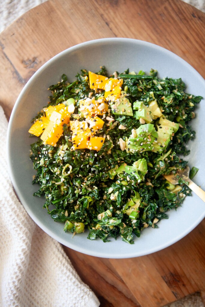 Chopped kale salad with toppings in white serving bowl with gold fork.