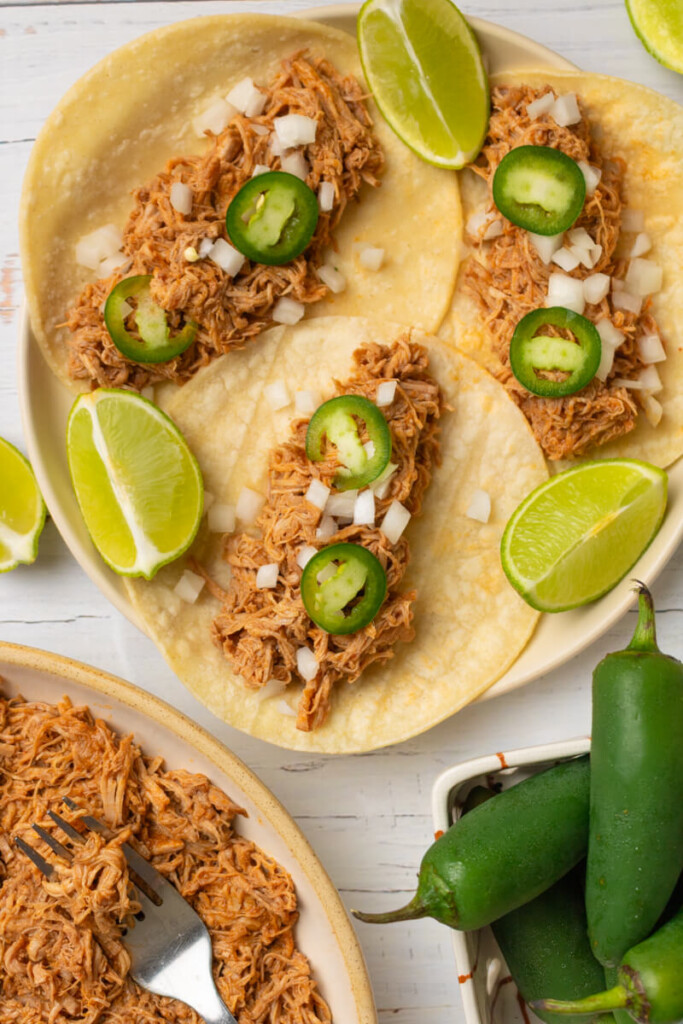 Red enchilada pork tacos on plate with lime slices.