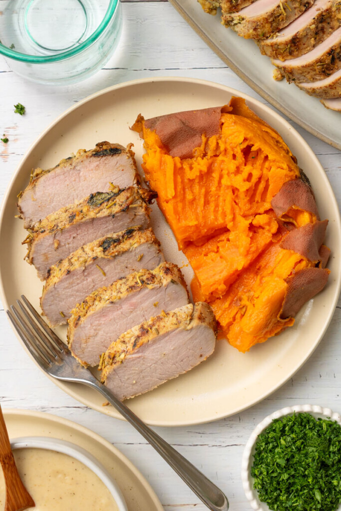 Slices of rosemary garlic pork tenderloin on plate with sweet potato and fork.