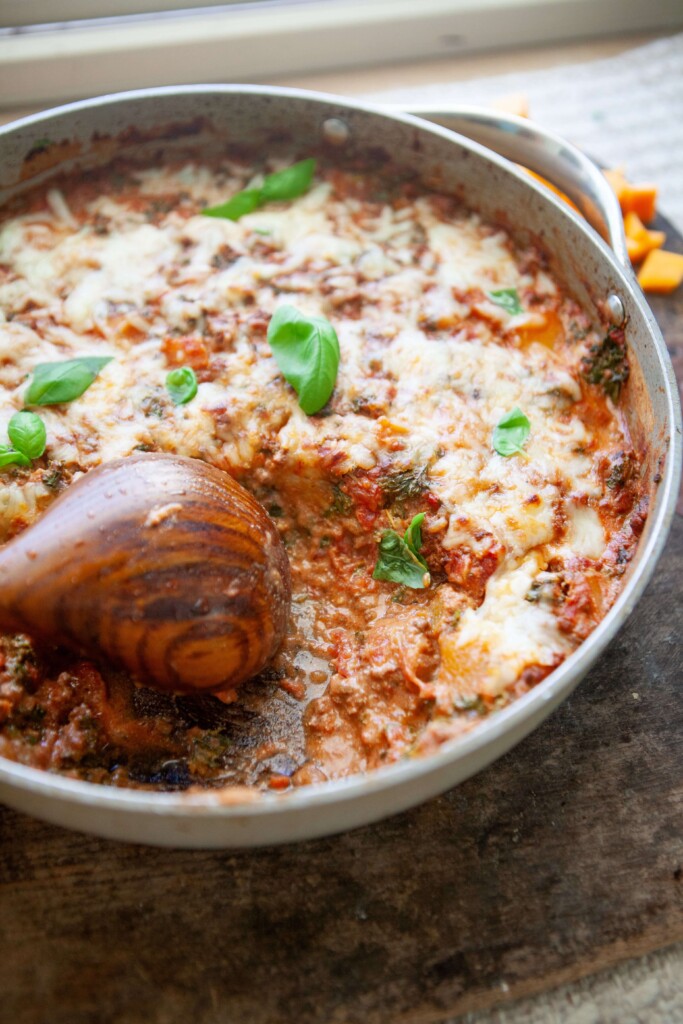 Butternut skillet lasagna garnished with fresh basil in metal skillet with wood spoon.