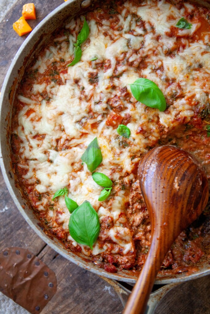 Butternut lasagna skillet meal in pan with wooden spoon on top of wood board.
