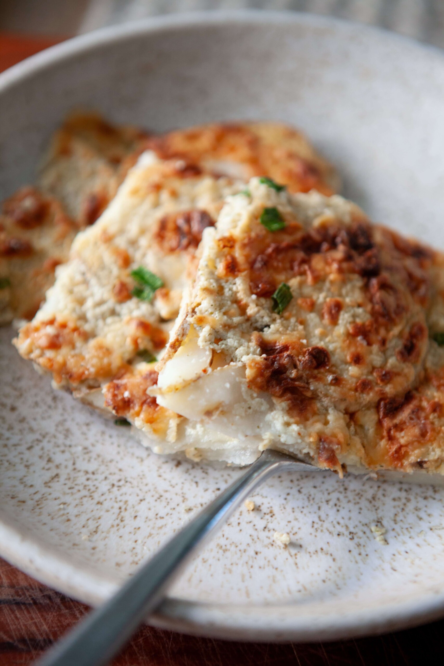 Stack of healthy scalloped potatoes on cream plate with fork.