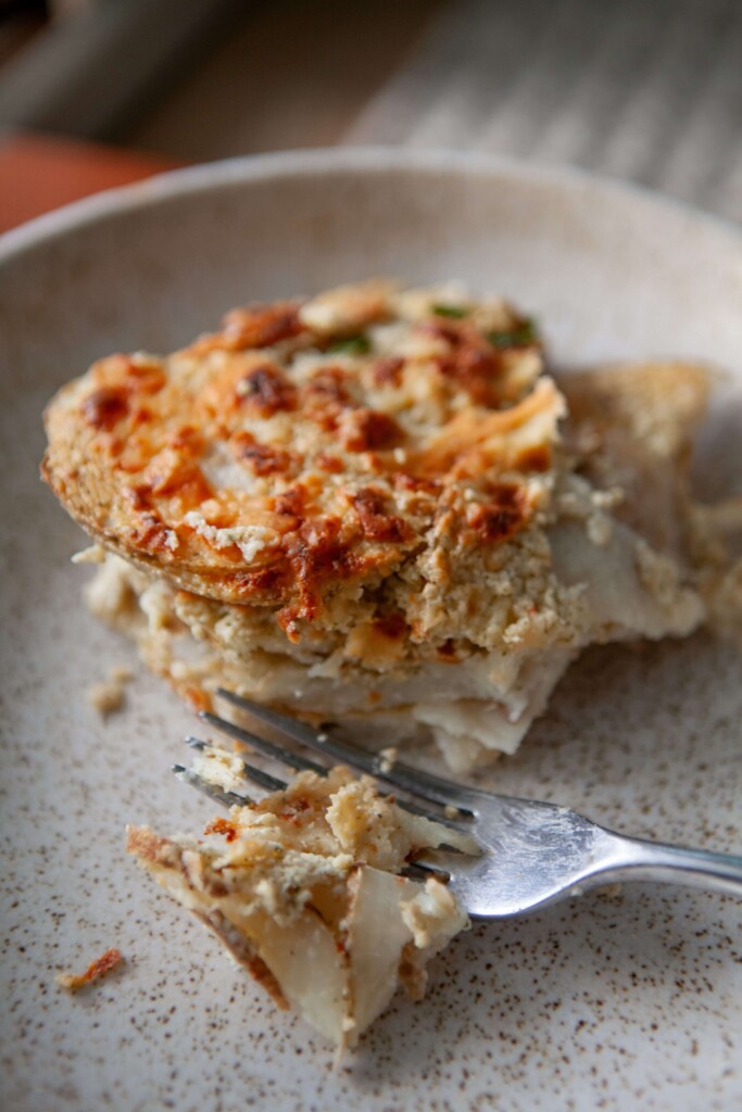 Fork breaking off a bite of scalloped potatoes on plate.