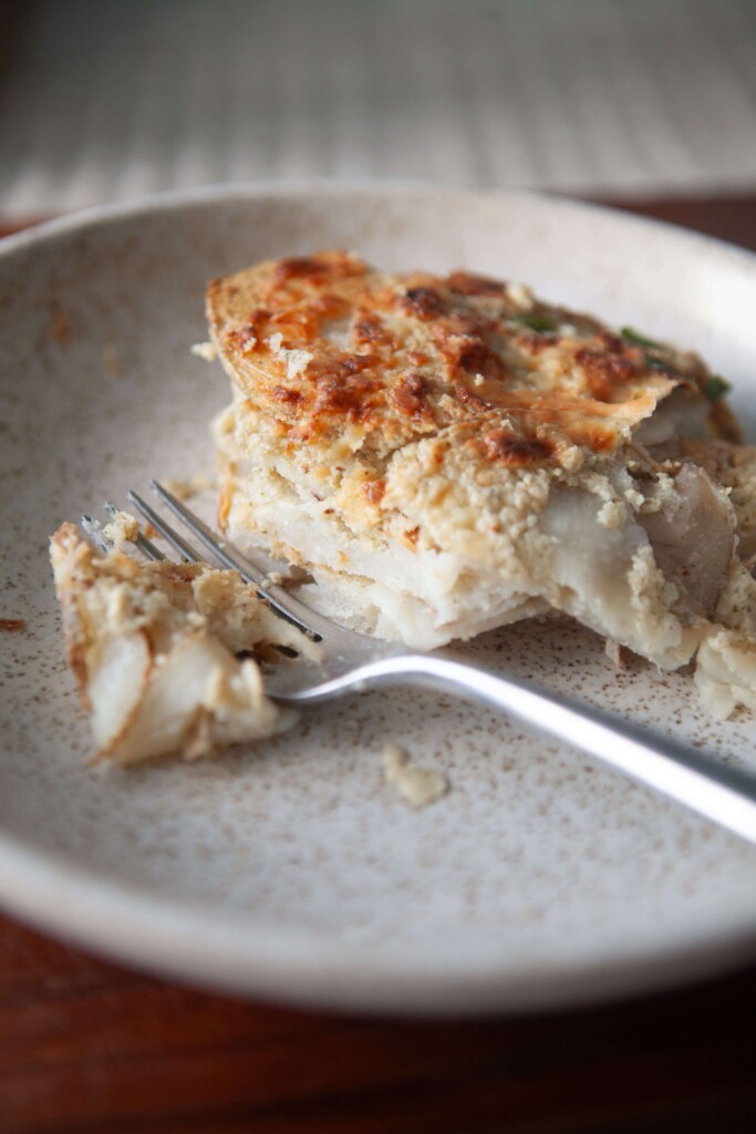 Healthy scalloped potatoes on cream plate with fork.