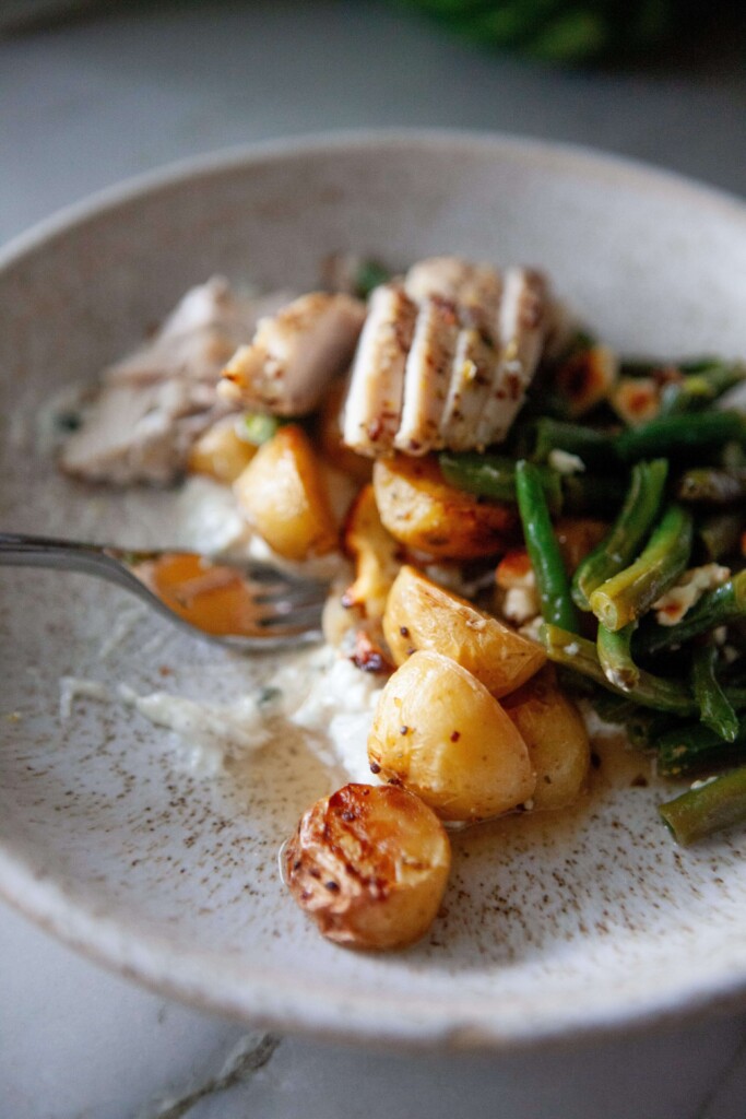 Bowl of lemon dijon chicken, green beans, and potatoes on top of tzatziki with fork.