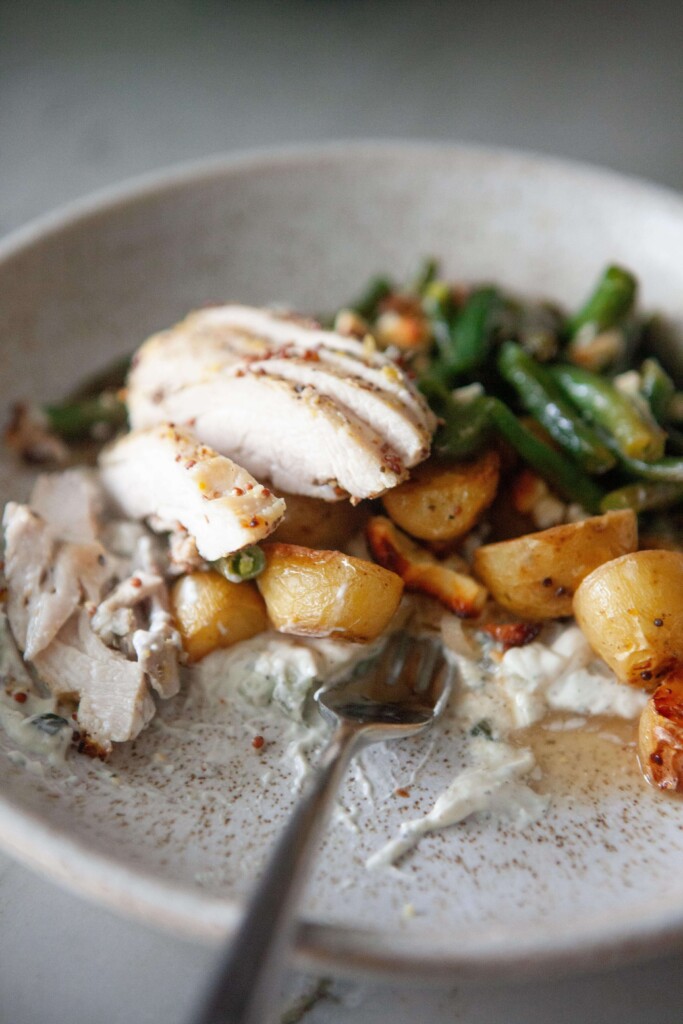 Bowl of chicken, green beans, and potatoes on top of tzatziki with fork.