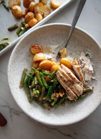 Chicken, green beans, and potatoes in bowl on top of tzaziki sauce with fork.