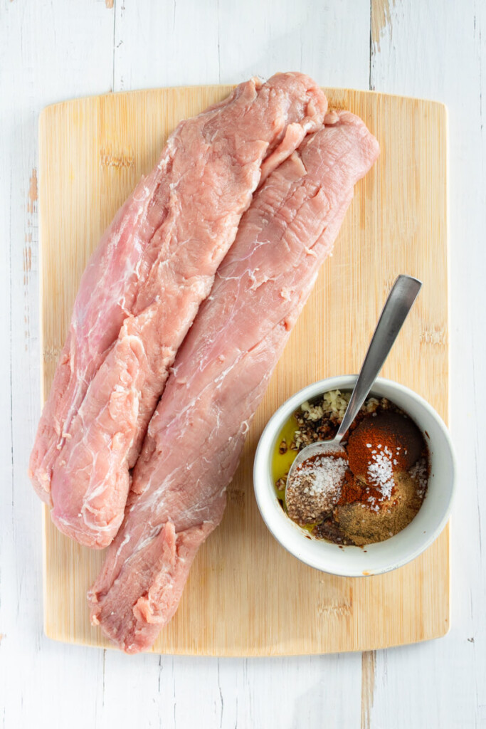 Mixing together rub ingredients in a small bowl on wood cutting board with two tenderloins.