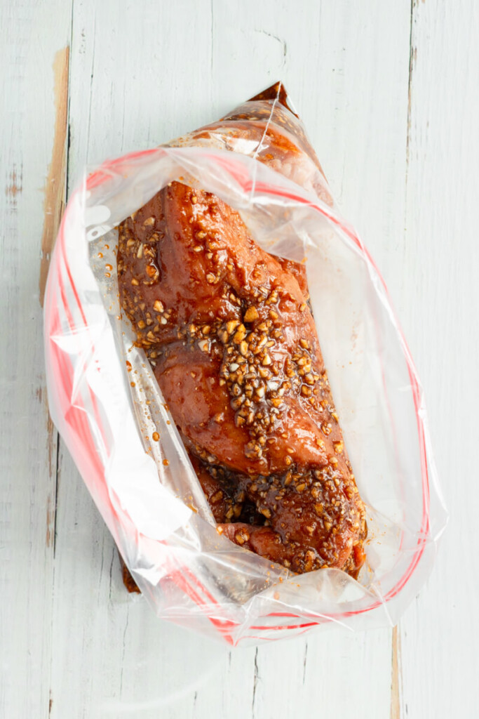 Pouring rub ingredients on top of pork tenderloins in ziplock bag.