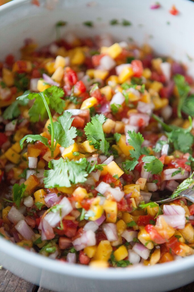 Mango salsa garnished with cilantro in white bowl on top of wood cutting board.