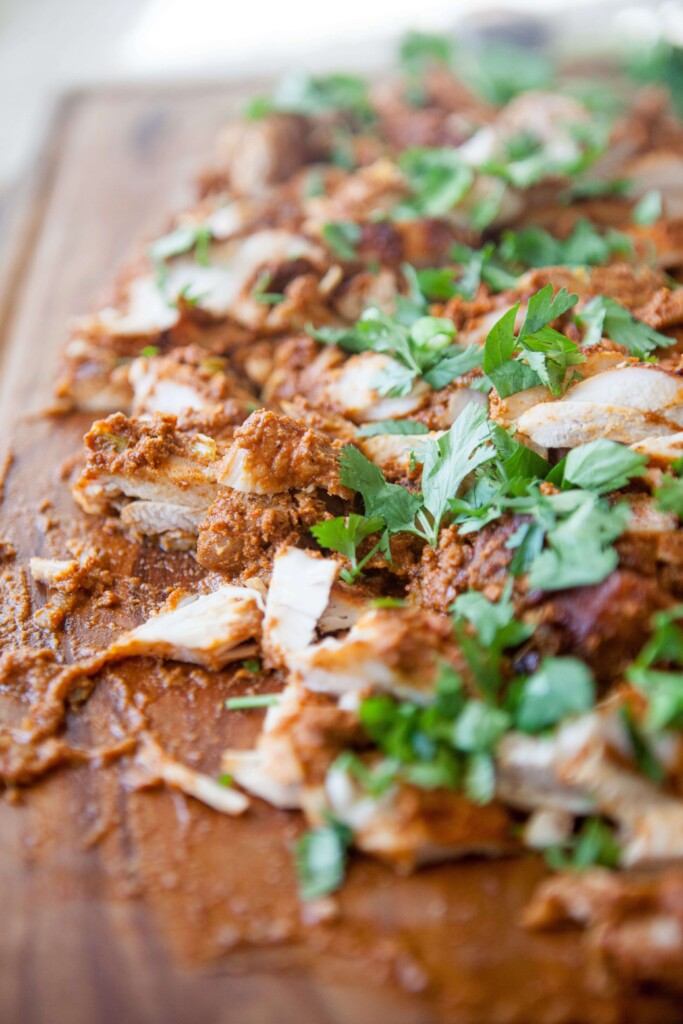 Mexican chicken thighs chopped up on a wooden cutting board garnished with cilantro.