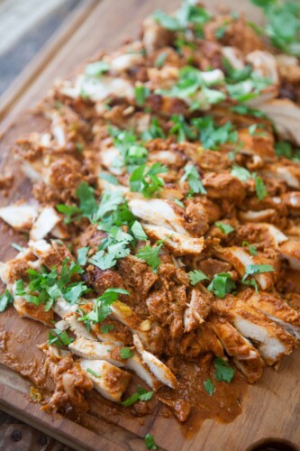 Mexican chicken thighs chopped up on a wooden cutting board garnished with cilantro.