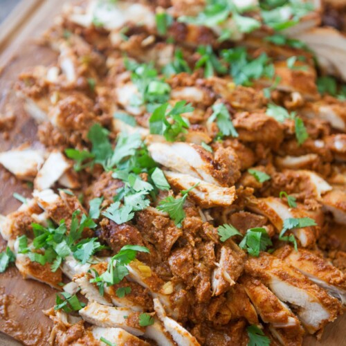 Mexican chicken thighs chopped up on a wooden cutting board garnished with cilantro.