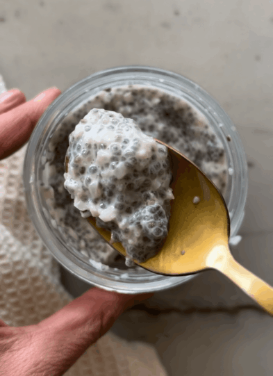 Bite of cauliflower chia pudding on gold spoon above glass jar.