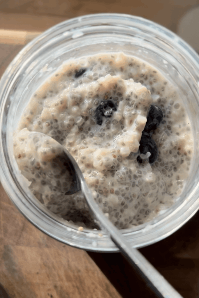 Cauliflower chia pudding mixed with fresh blueberries in a glass jar with a spoon.