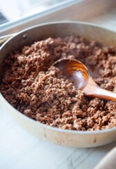 Classic taco meat cooked in large skillet with wood spoon in skillet.