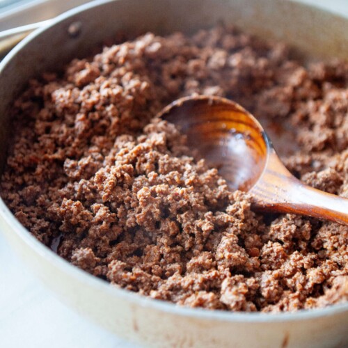 Classic taco meat cooked in large skillet with wood spoon in skillet.