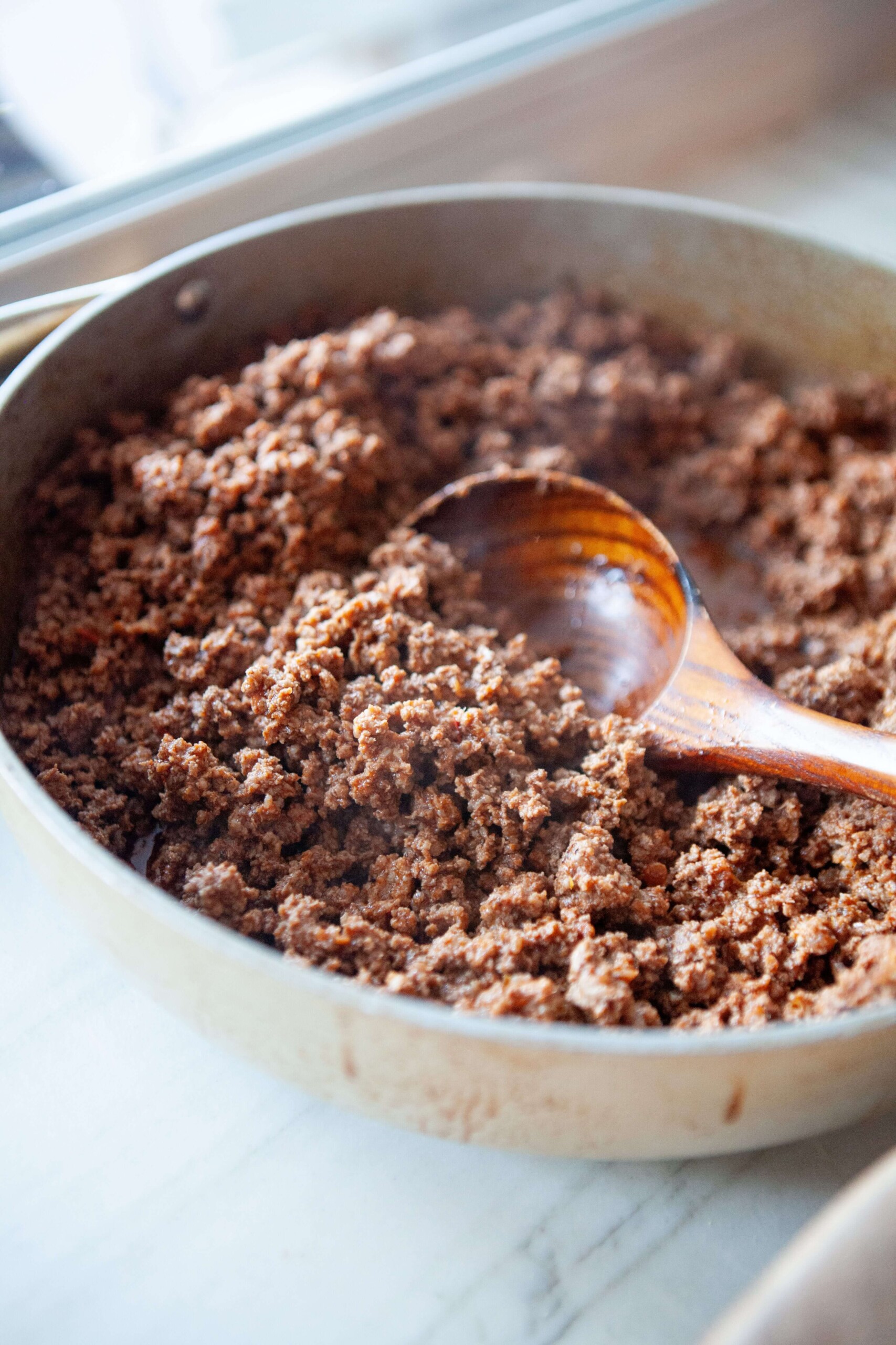Classic taco meat cooked in large skillet with wood spoon in skillet.