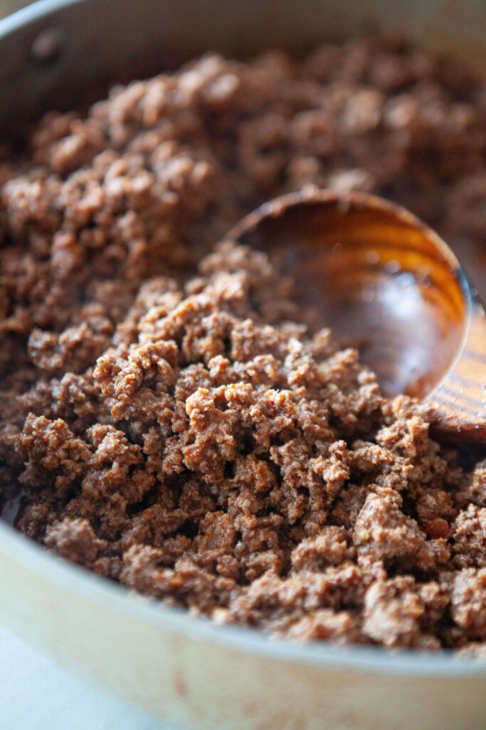 Cooked classic taco meat in large heavy-bottom skillet with wood spoon.