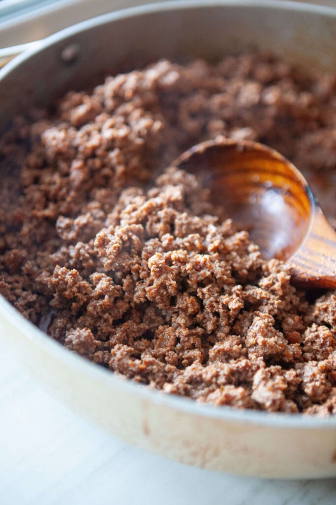 Cooked taco meat in large skillet with wood spoon.