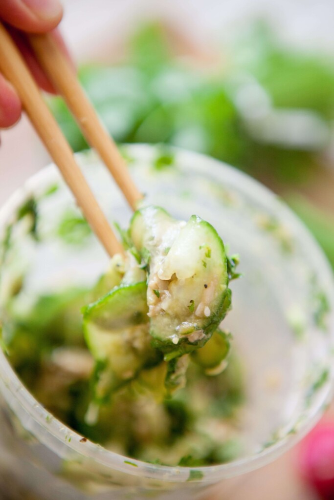 Chop sticks holding a bite of cucumber chicken salad out of plastic jar.