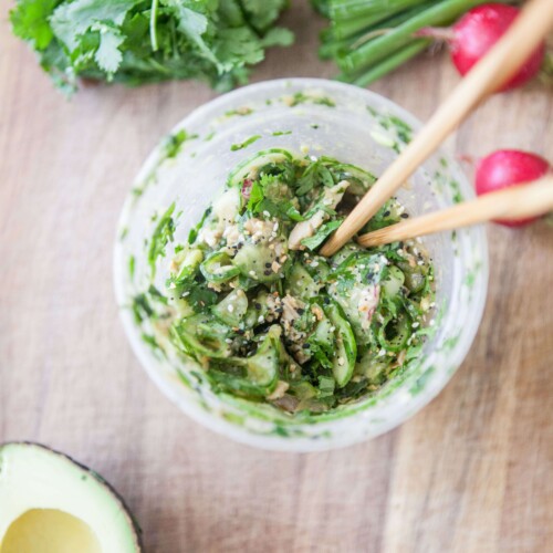 Pair of chopsticks in a plastic container of chicken avocado cucumber salad.