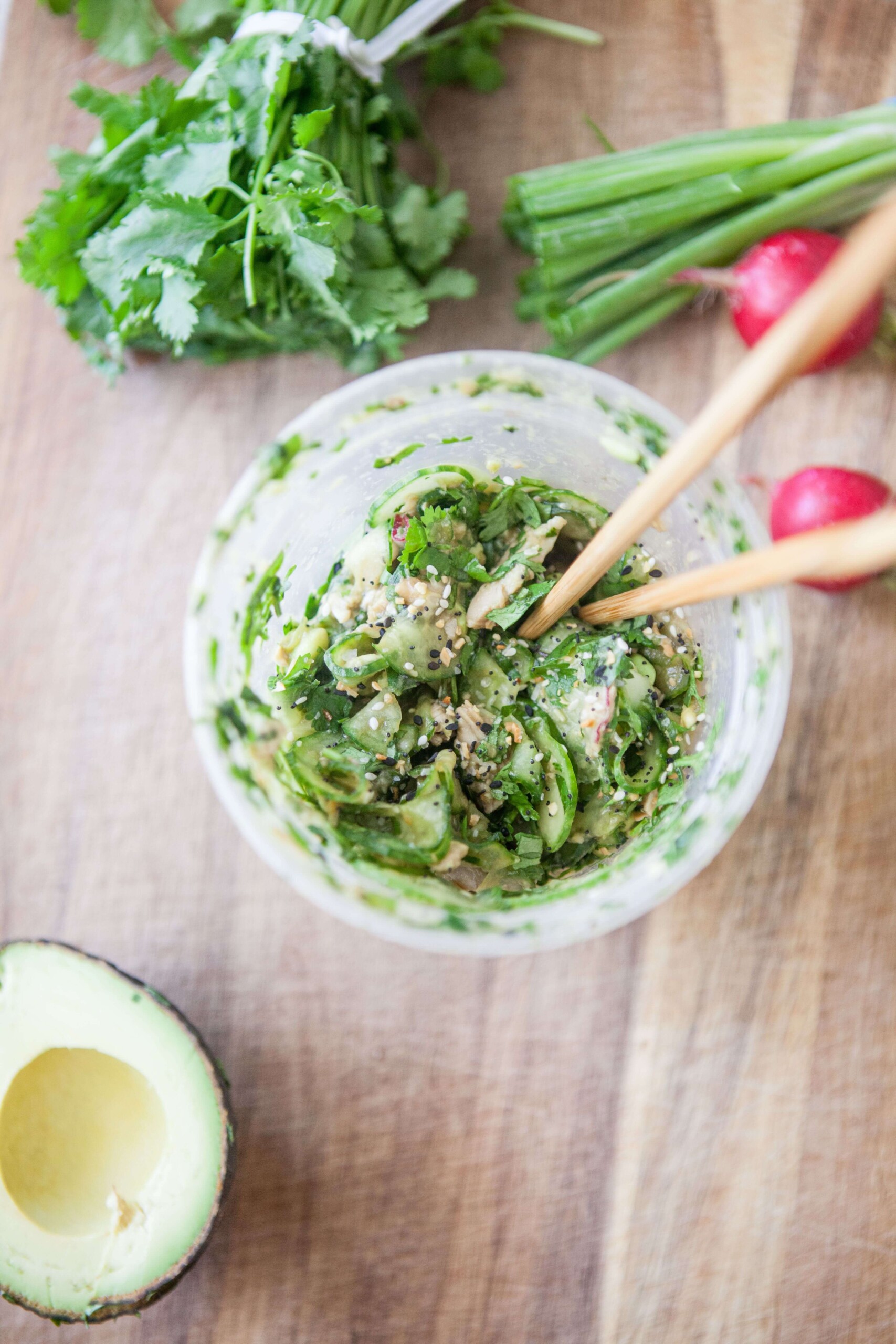 Pair of chopsticks in a plastic container of chicken avocado cucumber salad.