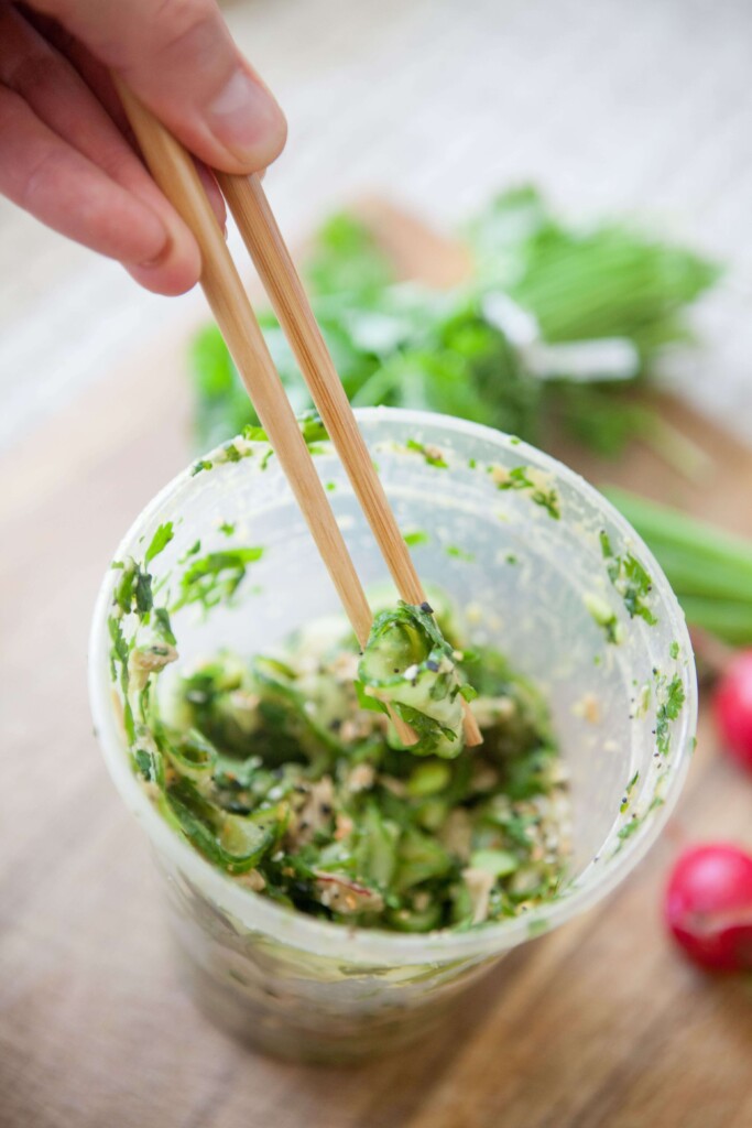 Easting cucumber chicken avocado salad out of a plastic container with chopsticks.
