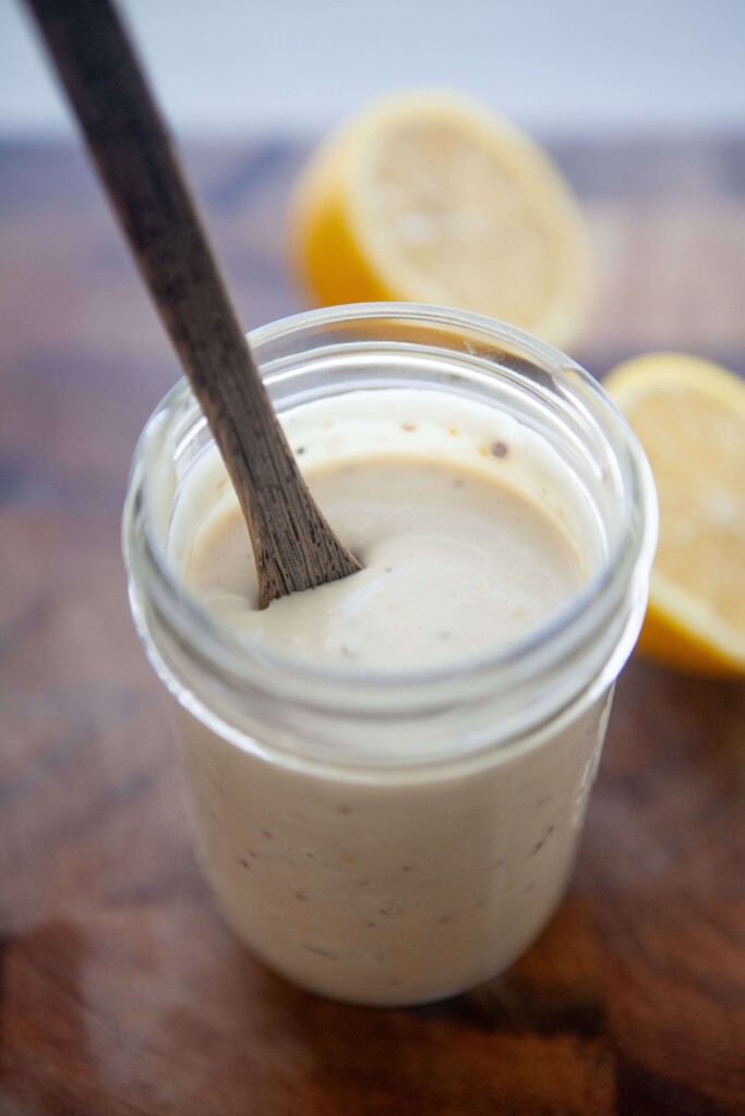 Greek yogurt caesar dressing in small mason jar stirred with wooden spoon.