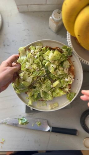 Caesar salad ground chicken pizza cut into four servings on white plate.